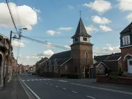 Plombier Oupeye près de l'église Saint-Laurent, rue animée avec maisons traditionnelles et services locaux.