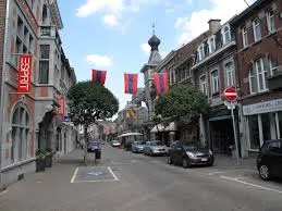 Rue animée de Visé avec bâtiment historique et véhicule de service Débouchage Visé garé près d'une fontaine centrale